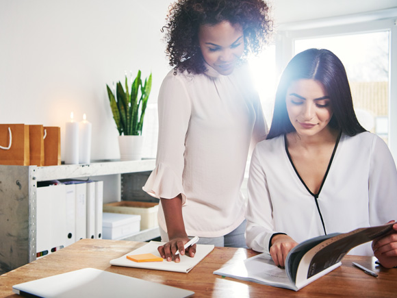 zwei Frauen sprechen über einen gedruckten Katalog