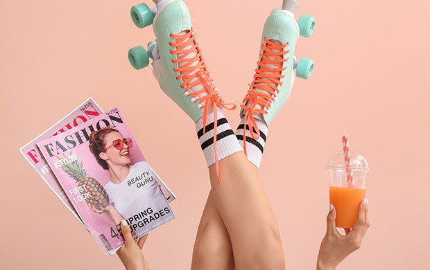 Zu sehen sind die Füße einer Frau, Rollschuhe an, in einer Hand eine Modezeitschrift, in der anderen ein gekühltes Getränk. Alles ist in knalligen Farben gehalten.