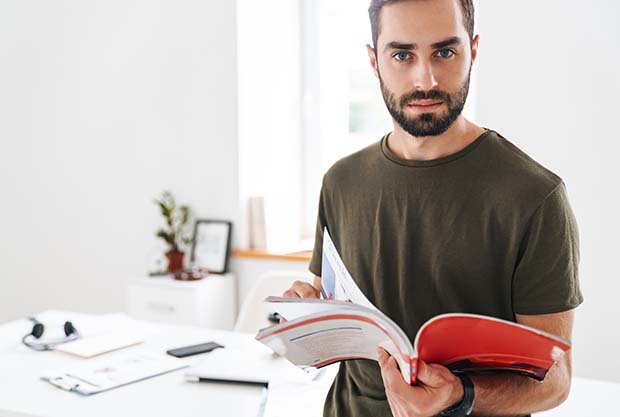 ein Mann hält einen Katalog mit Klebebindung in der Hand und sucht darin